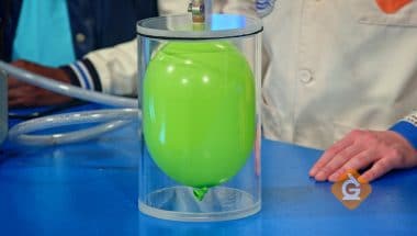 green balloon inflates inside of a vacuum chamber